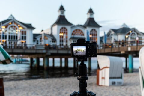 Reisestativ mit Kamera am Strand, im Hintergrund eine Seebrücke.