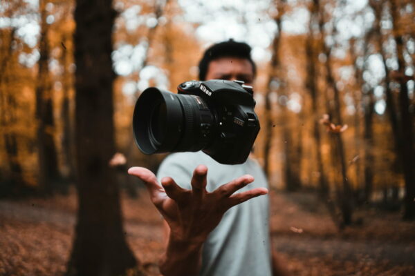 Person wirft eine Kamera in einem herbstlichen Wald in die Luft, symbolisiert Kreativität in der Fotografie.