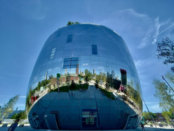 Futuristisches Gebäude mit spiegelnder Fassade, reflektiert die Umgebung unter klarem Himmel.