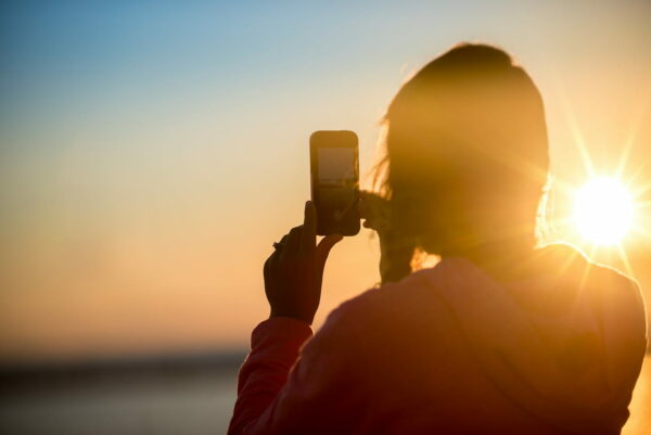 Frau fotografiert Sonnenuntergang mit Smartphone